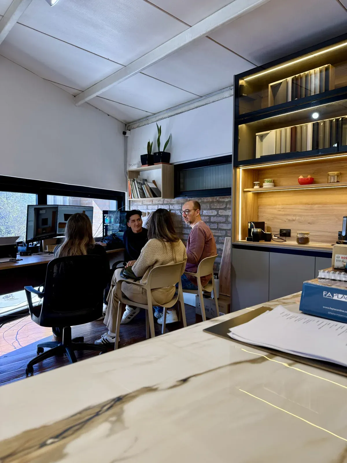 Asesoramiento con clientes en el escritorio de Brothers, con la mesa de mármol del showroom en primer plano