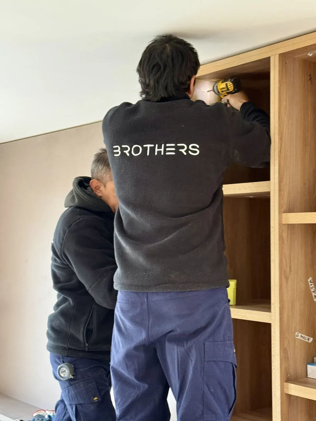 Dos instaladores de Brothers montan un placard de madera en la obra